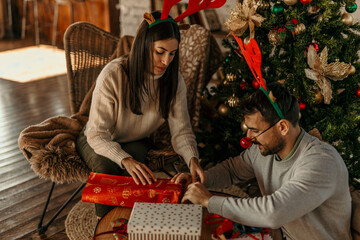 Shot of a happy young couple wrapping Christmas presents together at home. Teamwork and Christmas concept