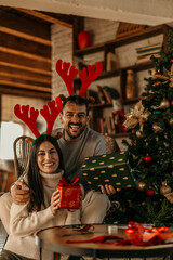 Couple sitting in the living room and celebrating Christmas holidays and holding gifts