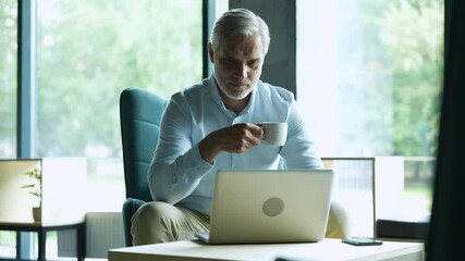 Wall Mural - Smiling businessman sitting in office lobby working on laptop. Male business professional working in office lobby.