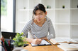© Fahng - Woman writing at cafe with laptop as university student for learning or online education. Female learner, happy and satisfied with studying or revision and research for college exams