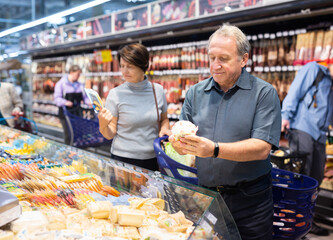 elderly male customer looking around in dairy section of supermarket