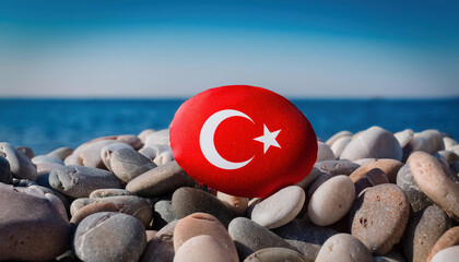 Wall Mural - A red painted pebble featuring the Turkish flag rests among beach pebbles against a backdrop of the blue sea.