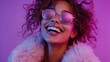 © Helois - A stylish woman with curly hair wearing sunglasses and a fur coat, laughing and looking up.