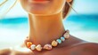 © Suphawan - Close-up of a shell necklace featuring small, colorful shells on a woman's neck, set against a tropical beach