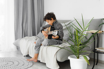 Preteen boy playing acoustic guitar dressed casual clothes, sitting on the cozy sofa at home living room. Music education concept image.