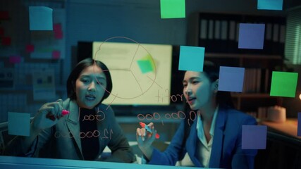 Aufkleber - Two businesswomen brainstorm and discuss strategy in a nighttime office setting, collaborating on a glass wall filled with notes and ideas for effective planning and innovation