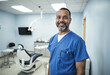 © RHL Studio - A smiling senior dentist in blue scrubs stands confidently in a modern dental clinic, showcasing professionalism and a welcoming atmosphere.