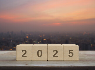 Wall Mural - 2025 letter on wood block cubes on wooden table over blur of cityscape on warm light sundown, Happy new year 2025 cover concept