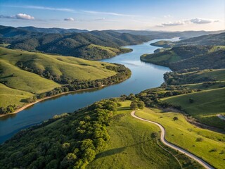 Wall Mural - Aerial View of a Winding River Flowing Through Lush Green Hills with a Serene Lake Nestled Amidst Rolling Terrain Capturing the Beauty of Nature and Tranquil Landscapes