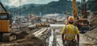 © kwangze - A construction worker oversees heavy machinery at a developing site under cloudy skies.