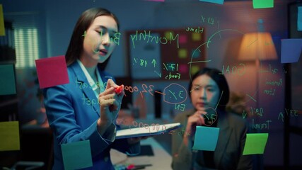 Poster - Businesswoman explains a marketing strategy to a colleague by writing on a glass wall in a modern office at night, surrounded by city lights and a collaborative atmosphere