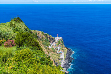 Wall Mural - A view over the headland towards the settlement and lighthouse at Arnel on the island of Sao Miguel in the Azores in summertime