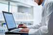 © Zape - A scientist analyzing data on a laptop while observing a laboratory experiment, emphasizing research in action. A researcher at work.