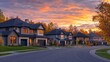 © Ruslan Gilmanshin - A picturesque suburban neighborhood at sunset, with modern homes lined along a curved street, warm lights glowing from windows, and vibrant autumn foliage under a colorful sky