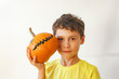 © Olga Gimaeva - Curly cute boy standing against white wall at cozy home and holding in his hands orange pumpkin with scary faces, happy halloween at home