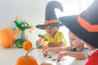 © Olga Gimaeva - Three real happy siblings two brothers and sister cutting together from real natural pumpkin jack o lantern, while playing with paper decorations of ghosts, children wearing with witch hats, halloween