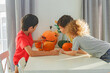 © Olga Gimaeva - Three real happy siblings two brothers and sister cutting together from real natural pumpkin jack o lantern, while playing with paper decorations of ghosts, children wearing with witch hats, halloween