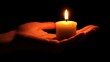 © ADIFERI - A single candle flame held in the palm of a hand against a black background.
