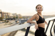 © BGStock72 - A joyful young woman enjoying music while exercising outdoors near a modern urban setting in the late afternoon light