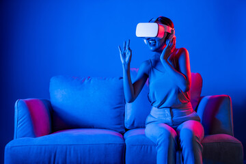 Sticker - Smart female sitting on sofa wearing VR headset connecting metaverse, future cyberspace community technology. Elegant woman enjoy gesticulate interacting another users in virtual world. Hallucination.