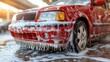 © Bejo Studio - Close-up of a red car covered in soap suds during a car wash.