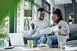 © peopleimages.com - Home, black couple and fist pump with paperwork on sofa for finance, savings and loan application success. Apartment, people and happy with documents on couch at lounge with credit card approval