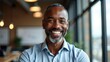 © useful pictures - A man with a confident smile is seated in a contemporary office, surrounded by natural light coming through large windows, showcasing a relaxed atmosphere