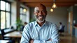 © useful pictures - A cheerful man with a beard smiles warmly while standing with arms crossed in a contemporary office. Sunlight filters through large windows, enhancing the inviting atmosphere