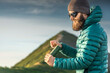 © XArt - Stylish bearded man wearing down jacket standing in front of a mountain peak and grinding coffee