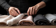 © SnowElf - Hands of a seamstress cutting fabric against the background of a table with various fabrics rolls. Tailor, atelier, custom tailoring, fabric store