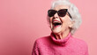 © Michael - Elderly woman in pink sweater and sunglasses smiling against pink backdrop