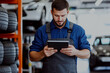 © Oksana - Mechanic in uniform uses a tablet in a garage surrounded by tires. Concept of technology in automotive repair.