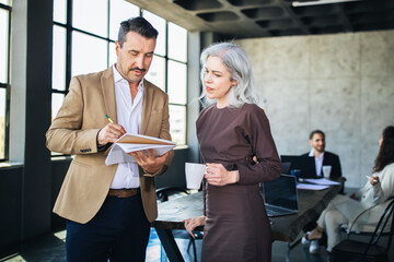 Fototapete - Two colleagues engage in a focused discussion while reviewing notes in a contemporary office. Others work in the background, contributing to a collaborative atmosphere.