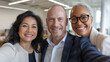 © Tom - A diverse group of professionals, including a South Asian woman, a Caucasian man, and an African American woman, smiling together in a modern office.