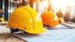 © ALIF JATI KUSUMA - Two yellow hard hats on blueprints with blurred background of construction workers.