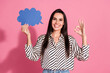 © deagreez - Confident young woman with brunette hair holding a speech bubble and gesturing okay against pink background in casual style