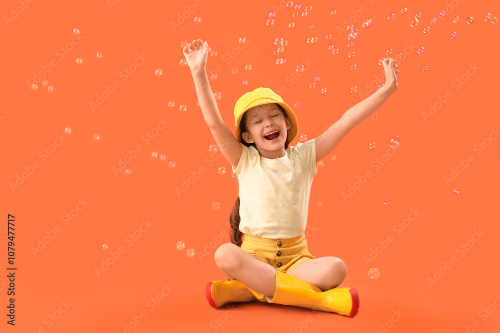 Happy little girl with soap bubbles on orange background