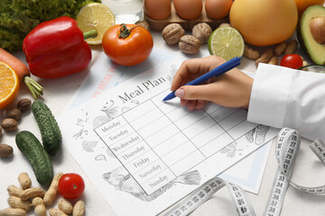 Wall Mural - Female nutritionist writing diet plan near healthy food on table