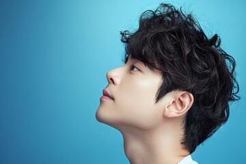 Profile view of young man, curly hair, looking upward isolated on blue, peaceful expression depicting tranquility concept