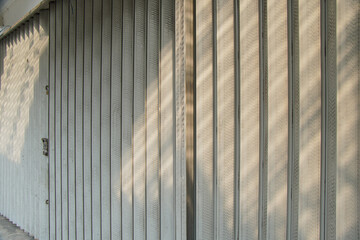 Poster - A close-up of a metal roll-up door with sunlight casting shadows on the surface. Sunlight casts long shadows on a closed metal gate. Close Up of a Metal Roll-Up Door