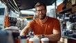 © LifeMedia - A bearded barista in a bright orange shirt smiles warmly while serving coffee in a cozy cafe, where an array of coffee-making equipment creates a bustling scene.