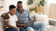 © Prostock-studio - Caring Black Grandfather Teaching His Preteen Grandson How To Use Computer, Sitting Together With Laptop On Couch In Living Room, Free Space