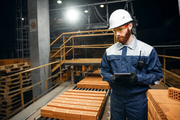 Wall Mural - Portrait man worker holding tablet computer for control quality of bricks. Production line of ceramics factory