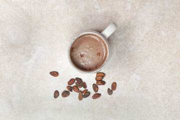 Hot cocoa drink in ceramic mug with cocoa beans around, view from above	