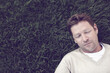 © peopleimages.com - Man, tired and sleeping on grass outdoor for resting, afternoon nap and exhausted in backyard. Calm person, face and dreaming on lawn at park with fatigue, relax and break with top view in nature