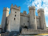 A medieval stone castle with towers and battlements under a blue sky.