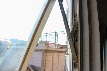 Poster - A view through a slightly open window revealing a glimpse of the building outside. Old rusty window showcasing the wear and tear of time. The background features a glimpse of the cityscape.