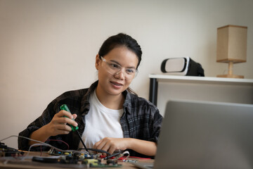 Canvas Print - A woman is sitting at a desk with a laptop and a toolbox. She is wearing safety glasses and she is working on a project