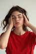 © Ева Поликарпова - A woman in a red shirt holds her head in her hands, possibly indicating pain or discomfort