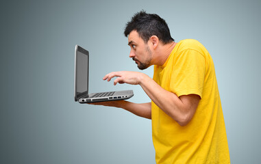 Portrait of an adult young man with a funny scruffy hairstyle holding a laptop in his hand. The hacker is concentrating on his computer. Programmer, user writing comments, working at a laptop.